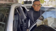 a man in a suit and sunglasses is getting out of a white car .
