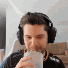 a man wearing headphones and a shirt that says twitch is drinking from a cup
