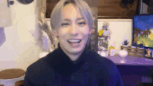 a young man with gray hair is smiling in a room with a teddy bear on a desk .