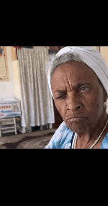 an elderly woman wearing a white turban and pearls is making a face