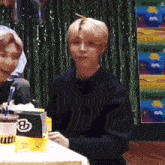 a man in a black sweater is sitting at a table in front of a sign that says butter .
