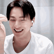 a young man wearing a white shirt and ear buds is smiling