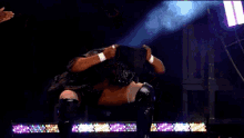 a wrestler wearing a mask is kneeling down on a stage in front of a crowd .