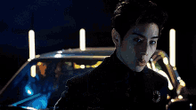a man in a black suit is standing in front of a car at night .