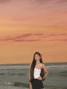 a girl with a flower in her hair is standing on the beach