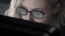 a close up of a woman wearing glasses looking at a computer screen