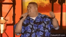 a man is singing into a microphone while wearing a blue shirt with flowers on it .