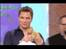 a man in a blue shirt is smiling and holding something in his hands