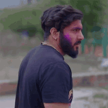 a man with a beard is wearing a black t-shirt and a chain around his neck