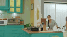a woman stands in a kitchen with turquoise cabinets and a stove top oven