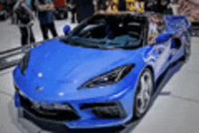 a blue sports car is parked on the side of the road in front of a crowd of people .