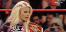 a woman is standing in a wrestling ring holding a wrestling belt .