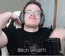 a man wearing headphones and glasses is sitting in front of a microphone and saying `` bitch what ? ''