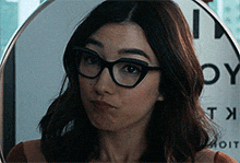 a woman wearing glasses is standing in front of a sign that says ' oy ' on it