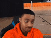 a young man in an orange hoodie is sitting in a chair .