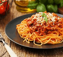 a black plate topped with spaghetti and meat sauce on a wooden table .