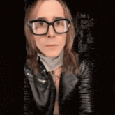 a woman wearing glasses and a leather jacket is wearing a mask around her neck .