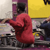 a man in a red sweater is running on a treadmill in a gym that says planet fitness on it