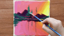 a person is painting a sunset over a lake with mountains in the background