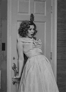 a woman in a dress is standing in front of a door holding the door handle .