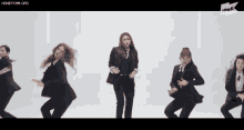 three women in suits are dancing in front of a white background and the url is honeycam.org