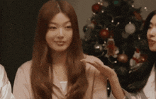 a woman in a pink shirt is standing in front of a christmas tree