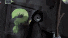 a cartoon character in a hooded cape is standing in front of a screen in a dark room .