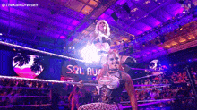 a woman is standing in a wrestling ring with a purple light behind her .