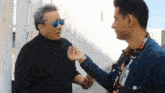 a man wearing sunglasses talks to another man wearing a name tag
