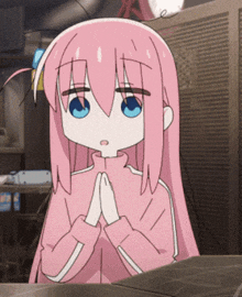 a girl with pink hair and blue eyes is sitting at a table with her hands folded