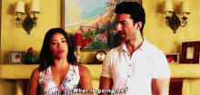 a man and a woman are standing next to each other and the woman is asking the man what is going on .