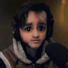 a young man wearing headphones and a vest is talking into a microphone and making a sad face .