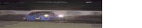 a blue car is driving down a race track at night .