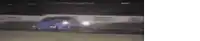 a blue car is driving down a race track at night .