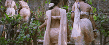 a group of women are walking through a forest and one of them has a flower in her hair