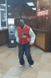 a man in a red varsity jacket is dancing in front of an atm machine