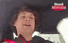 a man with curly hair is sitting in a car with the words good morning written on the bottom .