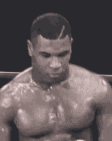 a man without a shirt is standing in a boxing ring in a black and white photo .