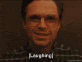 a close up of a man wearing glasses and a plaid shirt is laughing .