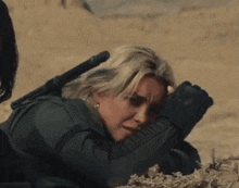 a woman laying on the ground with a rifle in her hand