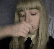 a woman with blonde hair and bangs is holding something in her mouth