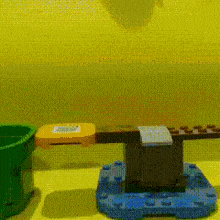 a green bucket and a blue block are on a table with a yellow wall in the background .