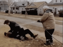a man in a tan jacket is spraying another man with a hose in front of a row of houses