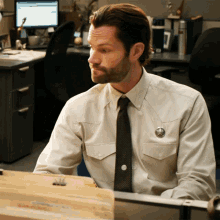 a man in a sheriff 's uniform sits at a desk in an office