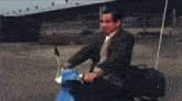 a man in a suit is riding a blue scooter with a bag on the back