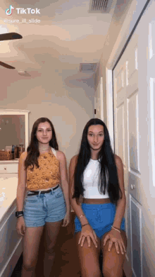 two girls are standing next to each other in a hallway with a ceiling fan in the background .