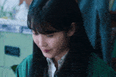 a woman with long black hair wearing a green jacket and a white shirt