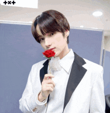a young man in a tuxedo holds a red rose in his mouth