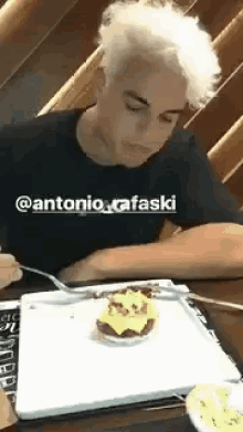 a man with white hair is sitting at a table with a plate of food and a fork .