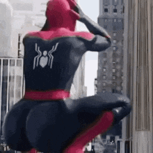 a man in a spiderman costume is kneeling down on a city street .